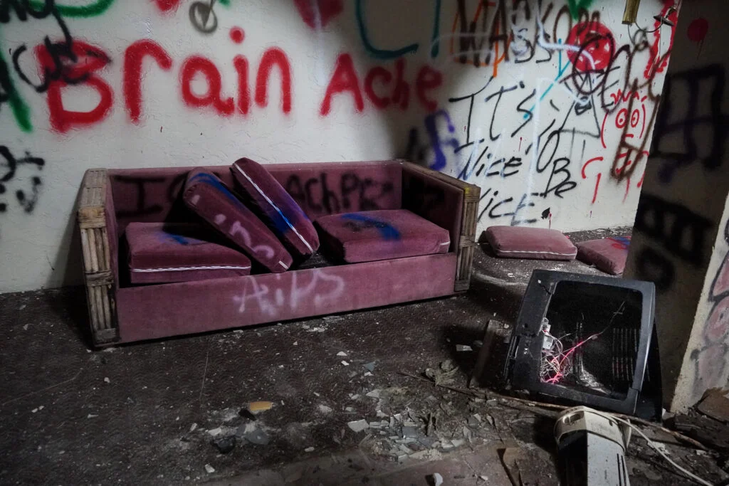 Graffiti-covered room inside the abandoned Port of the Islands Resort in Naples, Florida. A broken vintage television sits beside a vandalized purple couch with scattered cushions. The walls are covered in colorful graffiti, adding to the eerie, decayed atmosphere of this once-thriving Everglades getaway. Urban explorers and photographers visit this abandoned Florida hotel to capture its haunting beauty and history of neglect.